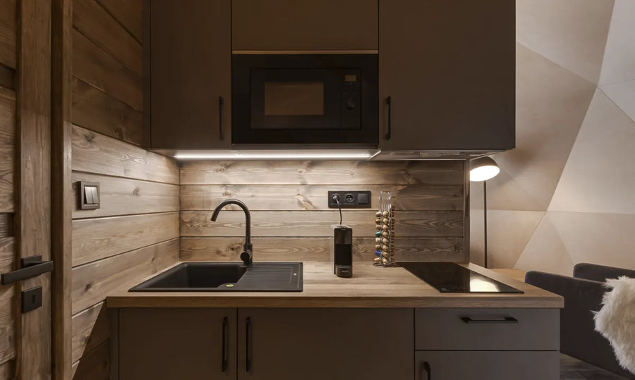 A compact kitchenette with a sink, cooktop and microwave inside a GeoHome