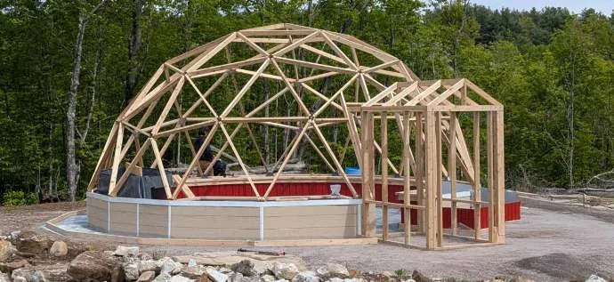 A timber dome frame part-way through assembly on its foundation